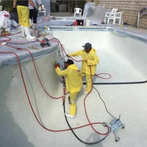 Workers polishing swimming pool walls with pneumatic equipment and connected hoses