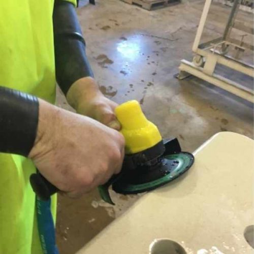 Worker using ALPHA PSC-600 Pneumatic Stone Cutter for wet grinding on stone