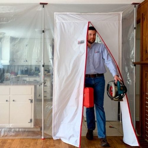Person entering through ZipDoor Magnetic Door Kit installed on a plastic dust barrier